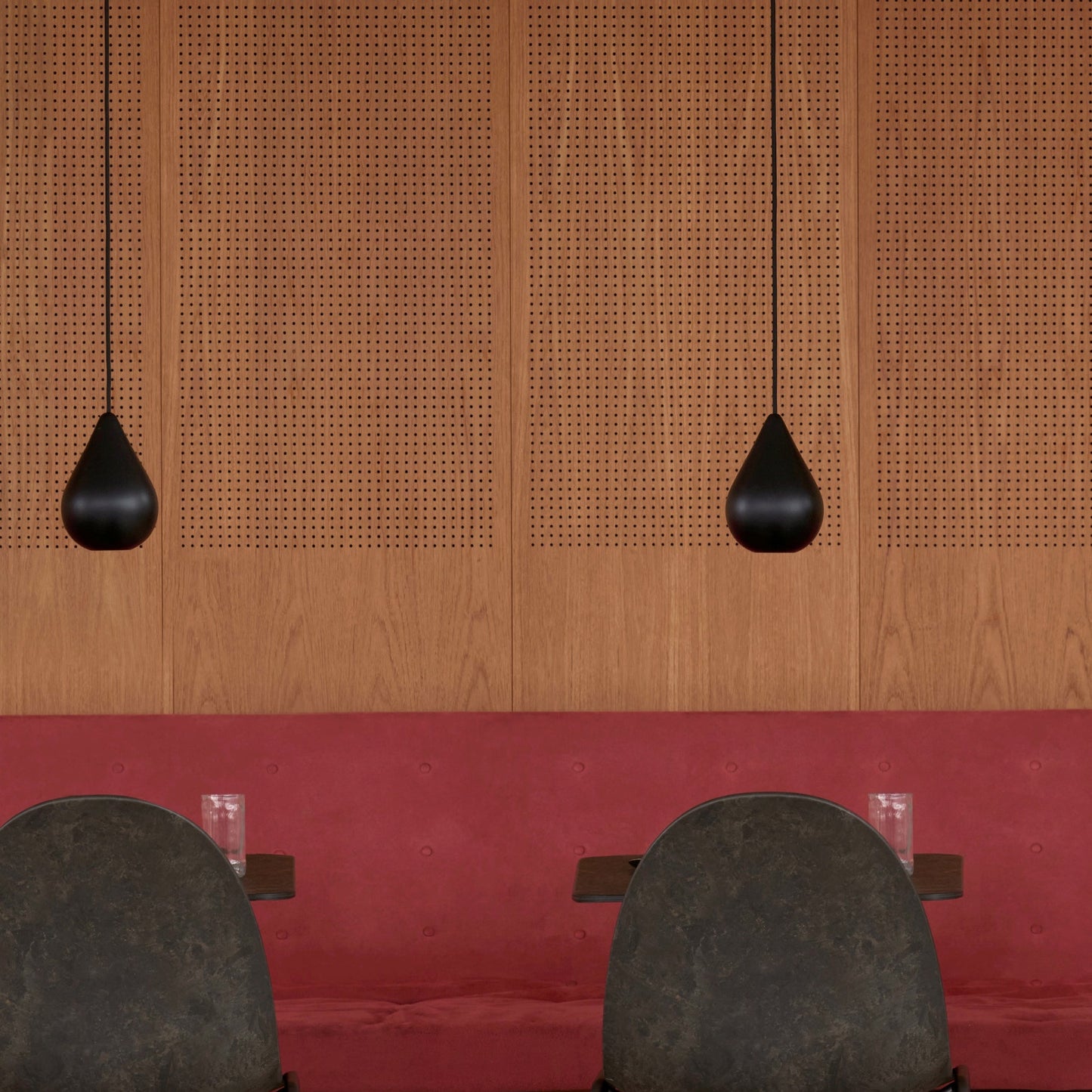 Two dark gray chairs in front of a wooden panel wall with two black pendant lights.