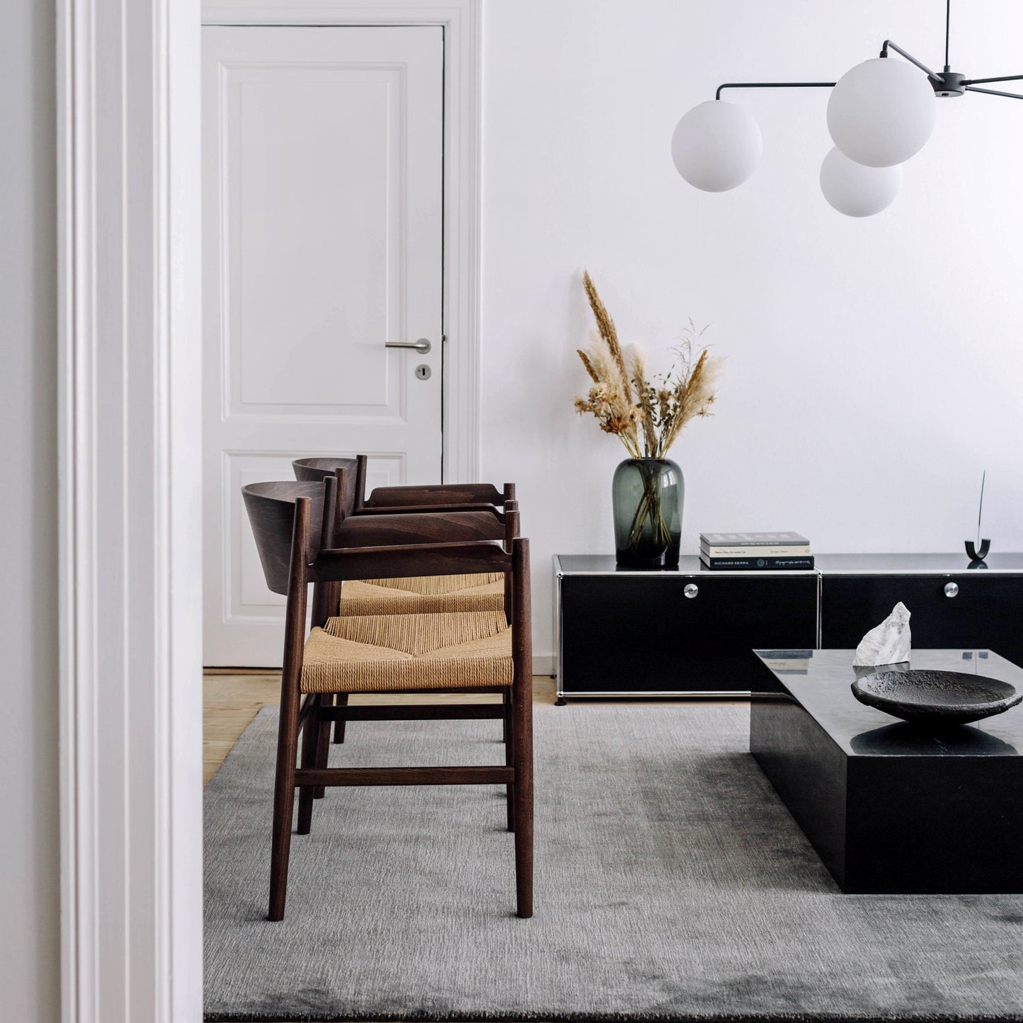 Modern living room with black coffee table, wooden chairs, and decorative elements.