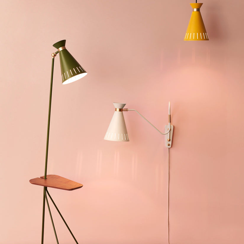 Three different lamps against a pink wall: a green floor lamp, a white wall-mounted lamp, and a yellow pendant lamp.
