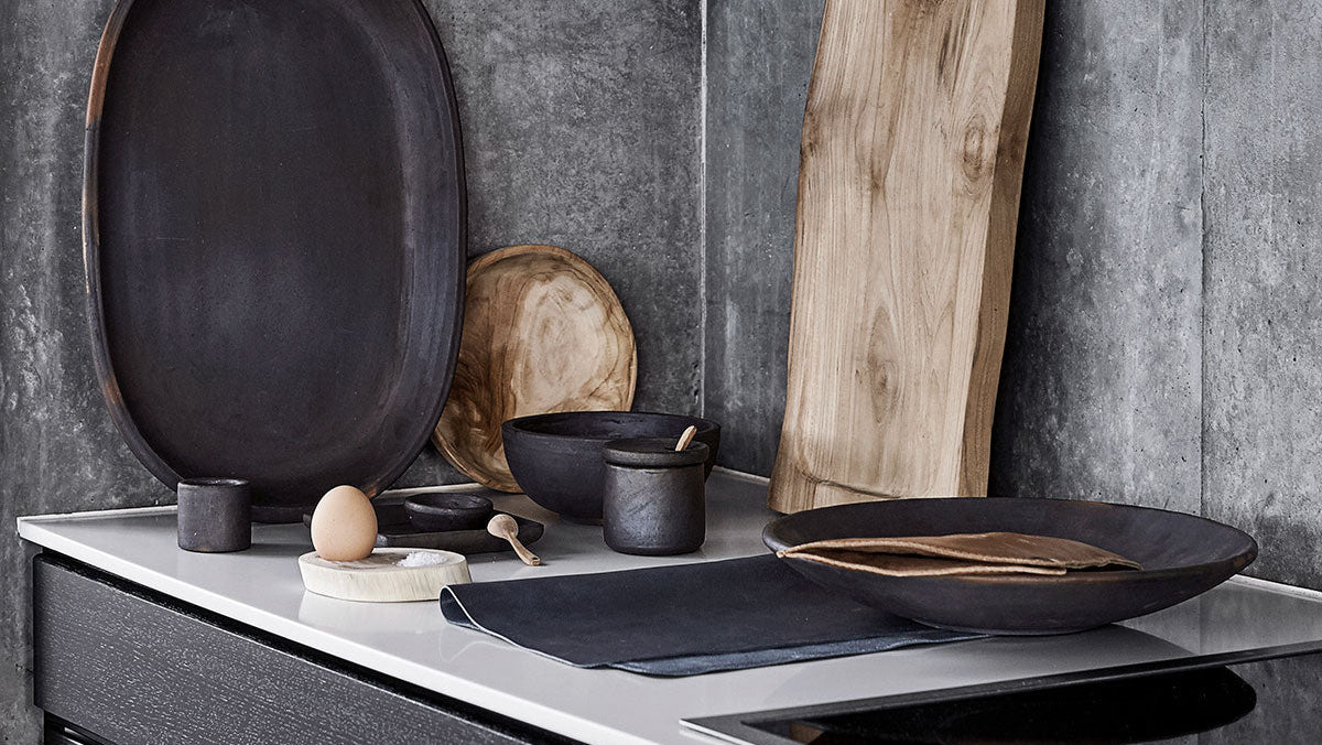 Black plates and wooden cutting board on a kitchen counter with a concrete wall background