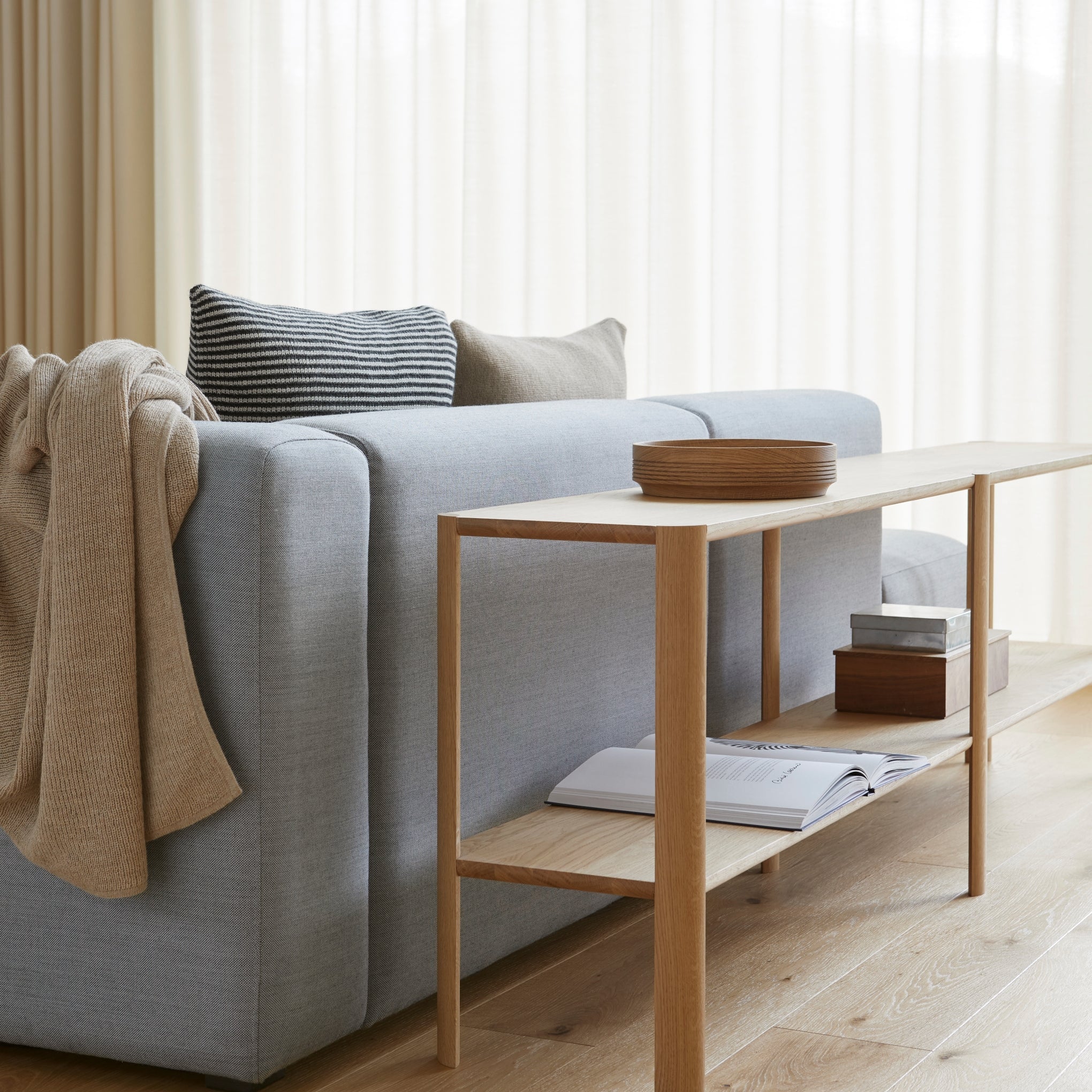 Modern living room with a gray sofa, wooden side table, and light decor.